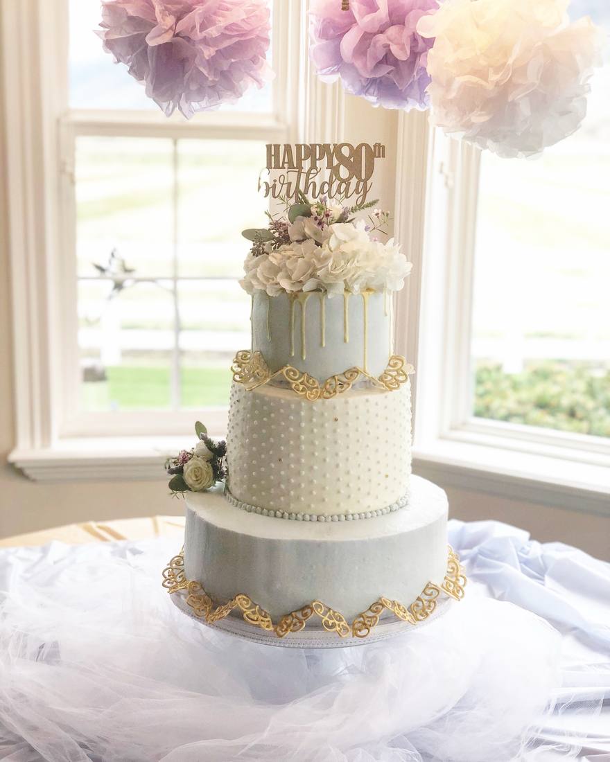 Elegant pale blue 80th birthday cake with gold filigree and hydrangeas