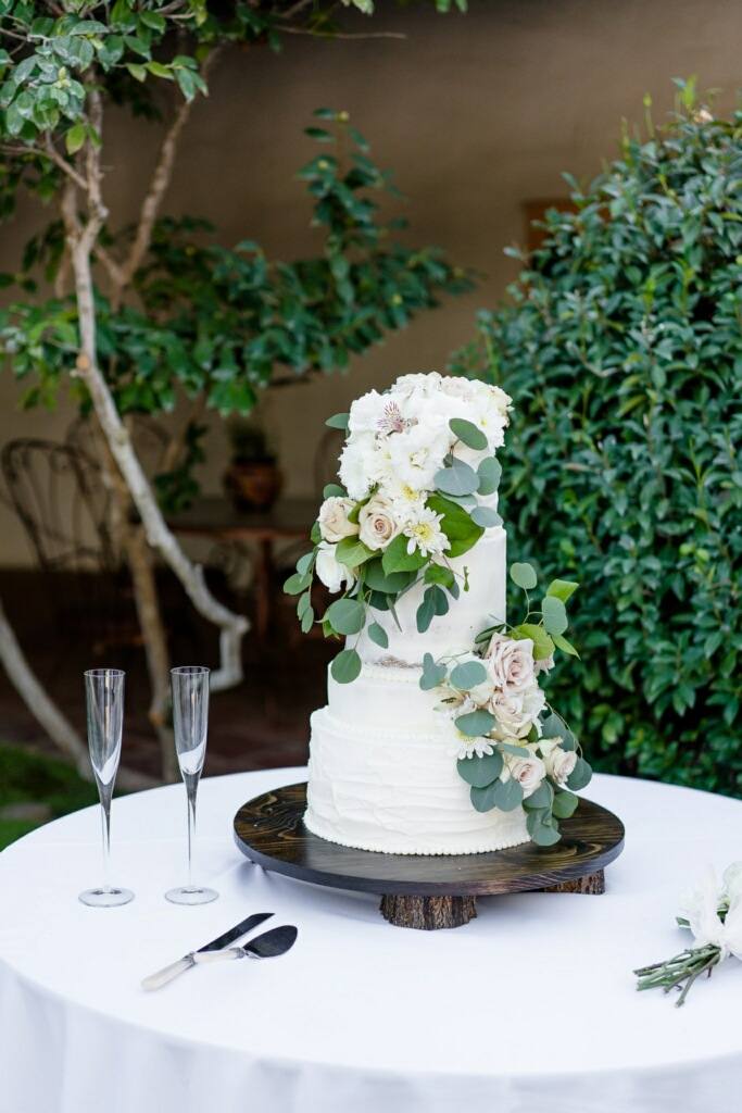 White tiered wedding cake with blush roses and eucalyptus in a garden setting