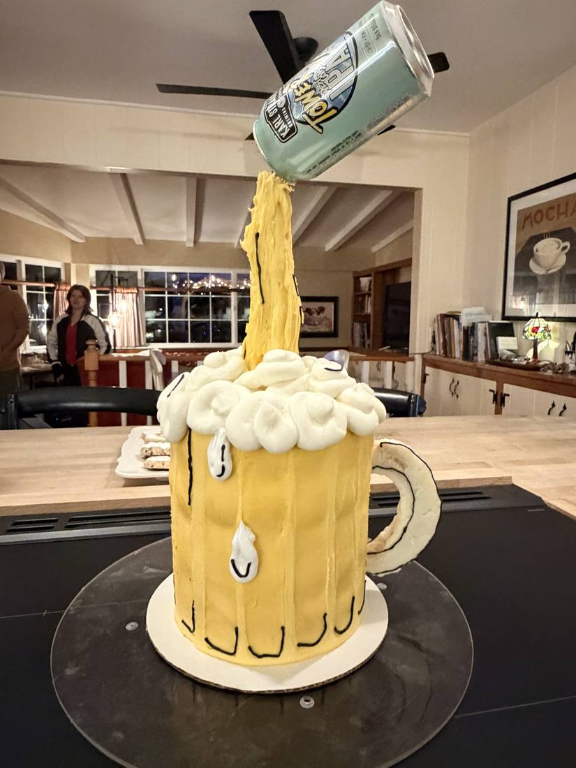 Sculpted beer mug cake with a gravity defying can pouring frosting into the foam
