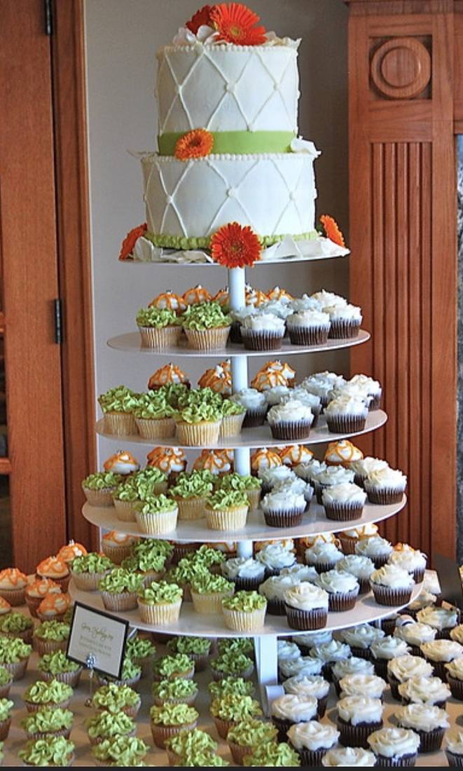 White tiered wedding cake with orange gerbera daisies atop a cupcake tower